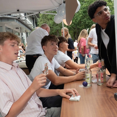 Zu jedem Zaubertrick geh&ouml;rt eine Geschichte &ndash; hier die vom Polizisten (K&ouml;nig) und den vier Bankr&auml;ubern, den Buben im Kartenspiel. Sch&uuml;ler aus der 10e schauen gebannt auf die Reaktion eines Schulfest-Besuchers.